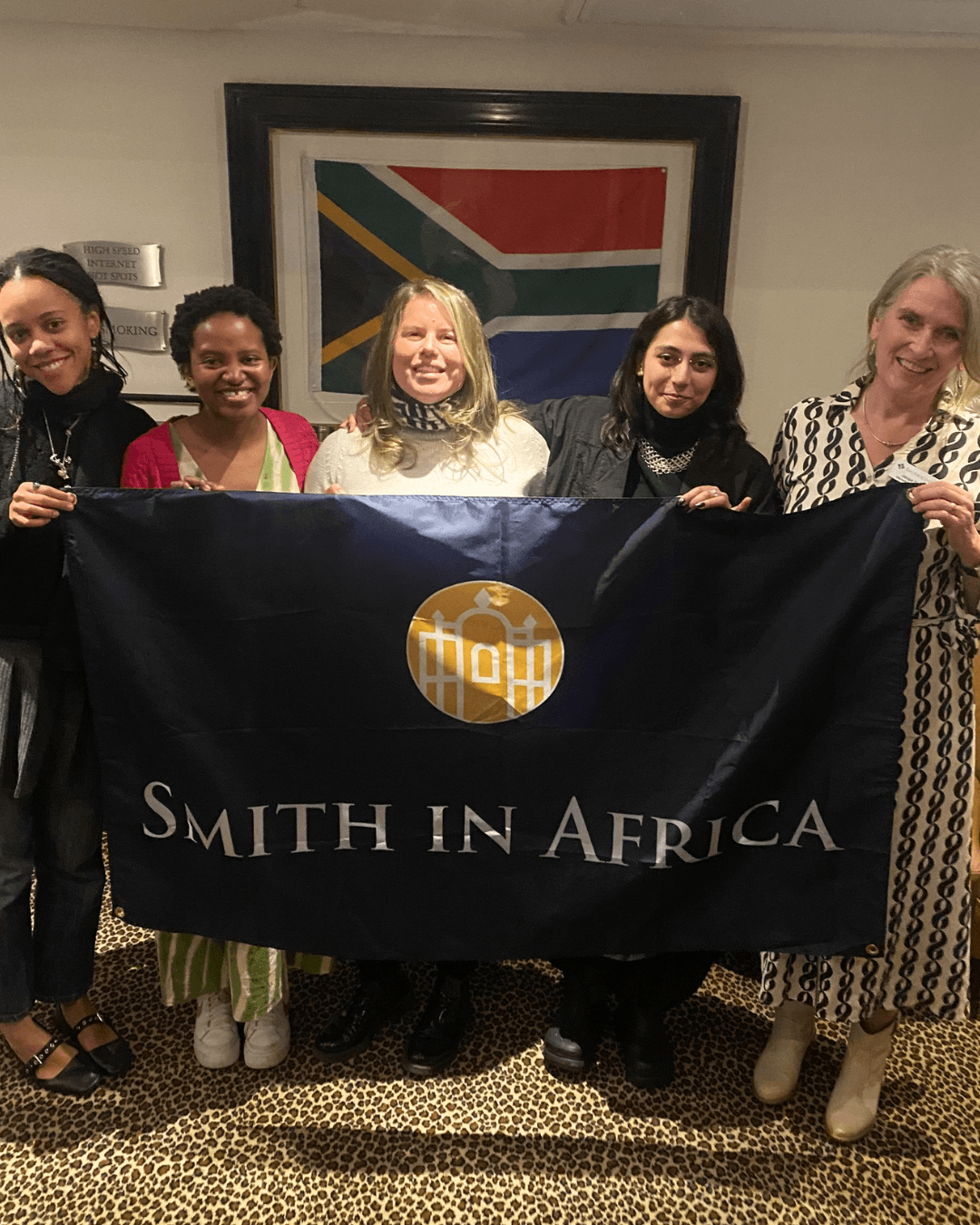 Five women holding a "Smith in Africa" banner in front of a South African flag.