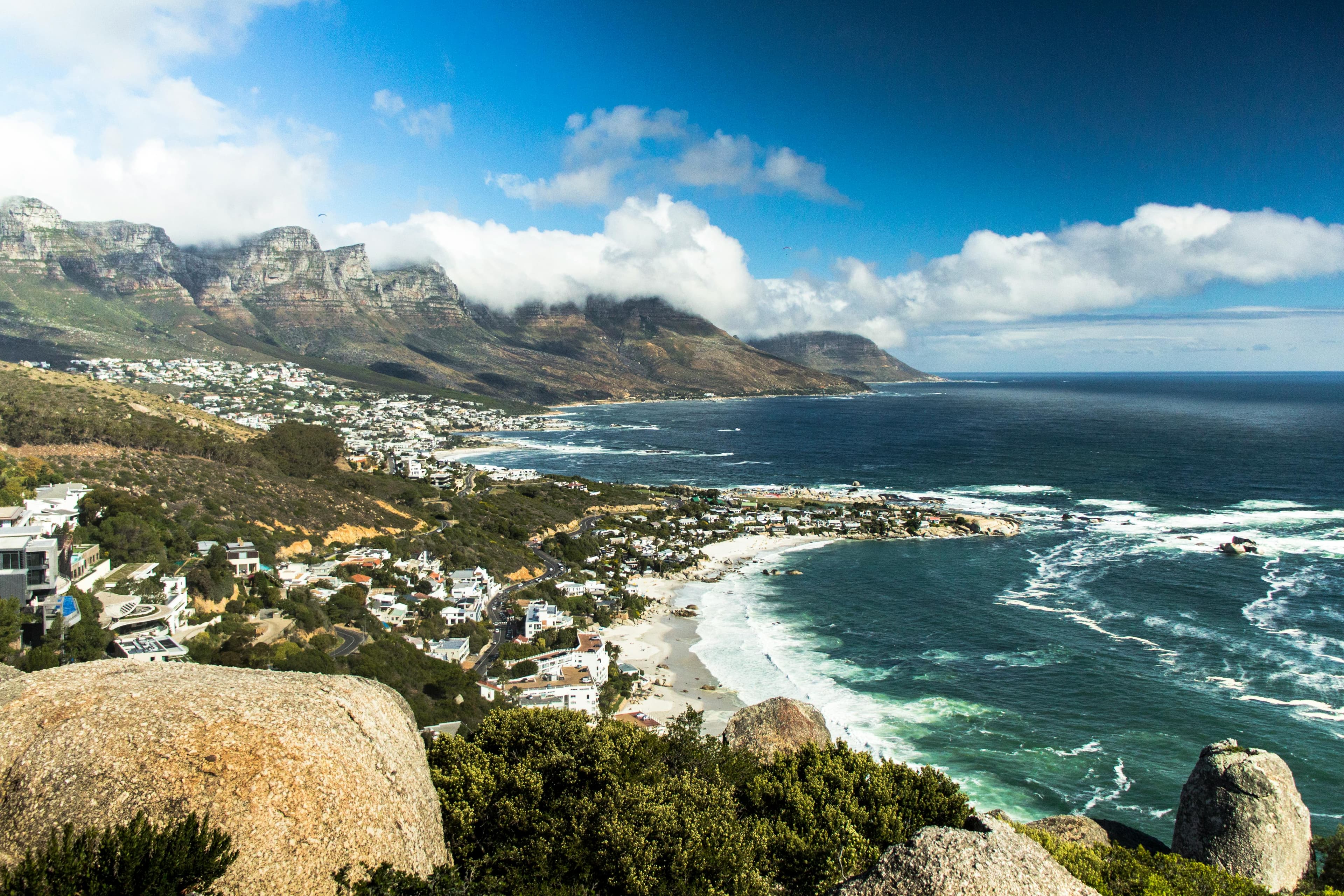 Coastal town nestled between rugged mountains and the deep blue ocean with crashing white waves.