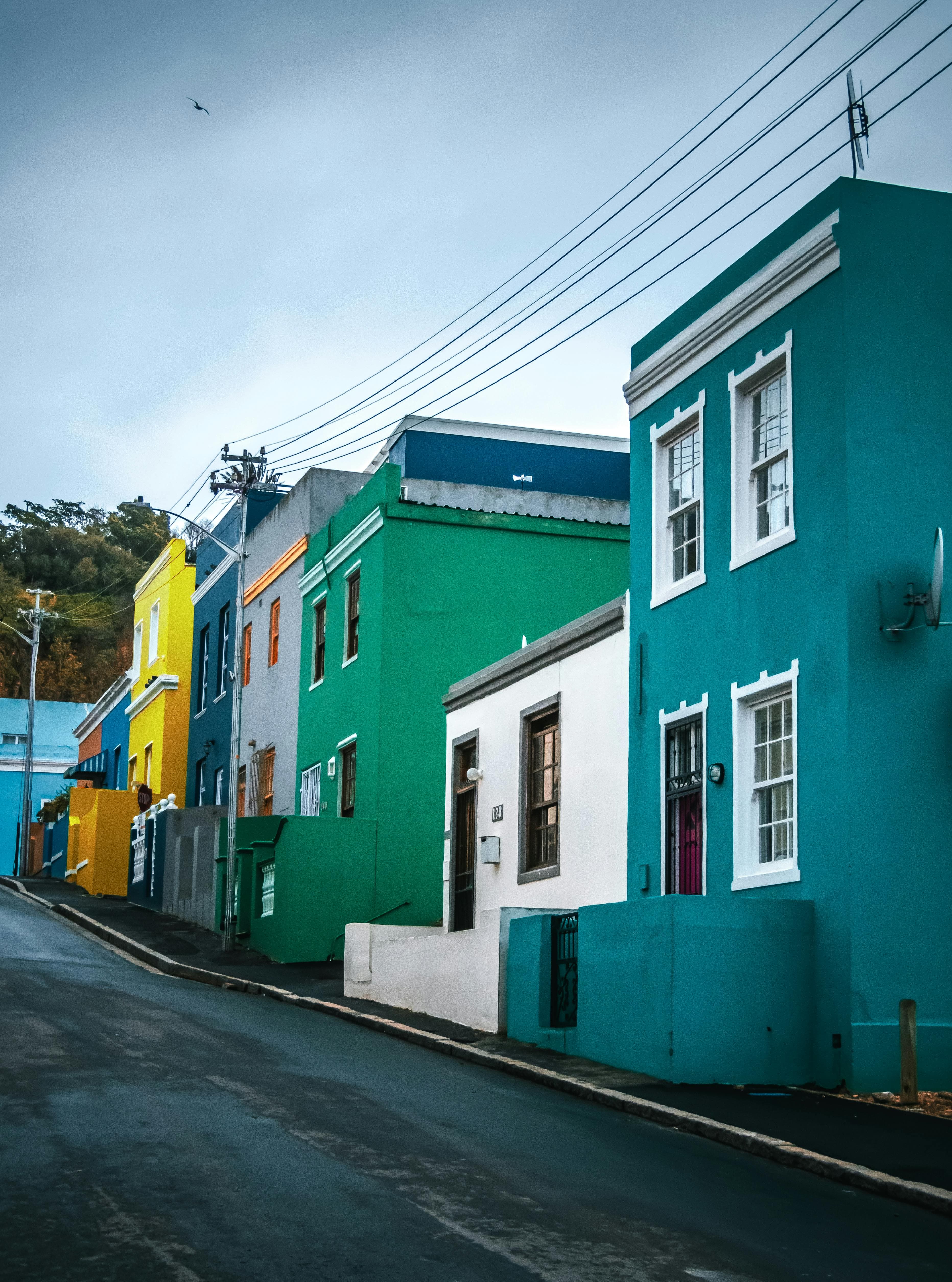 Vibrant teal, green, and yellow houses line a steep, wet street under an overcast sky.